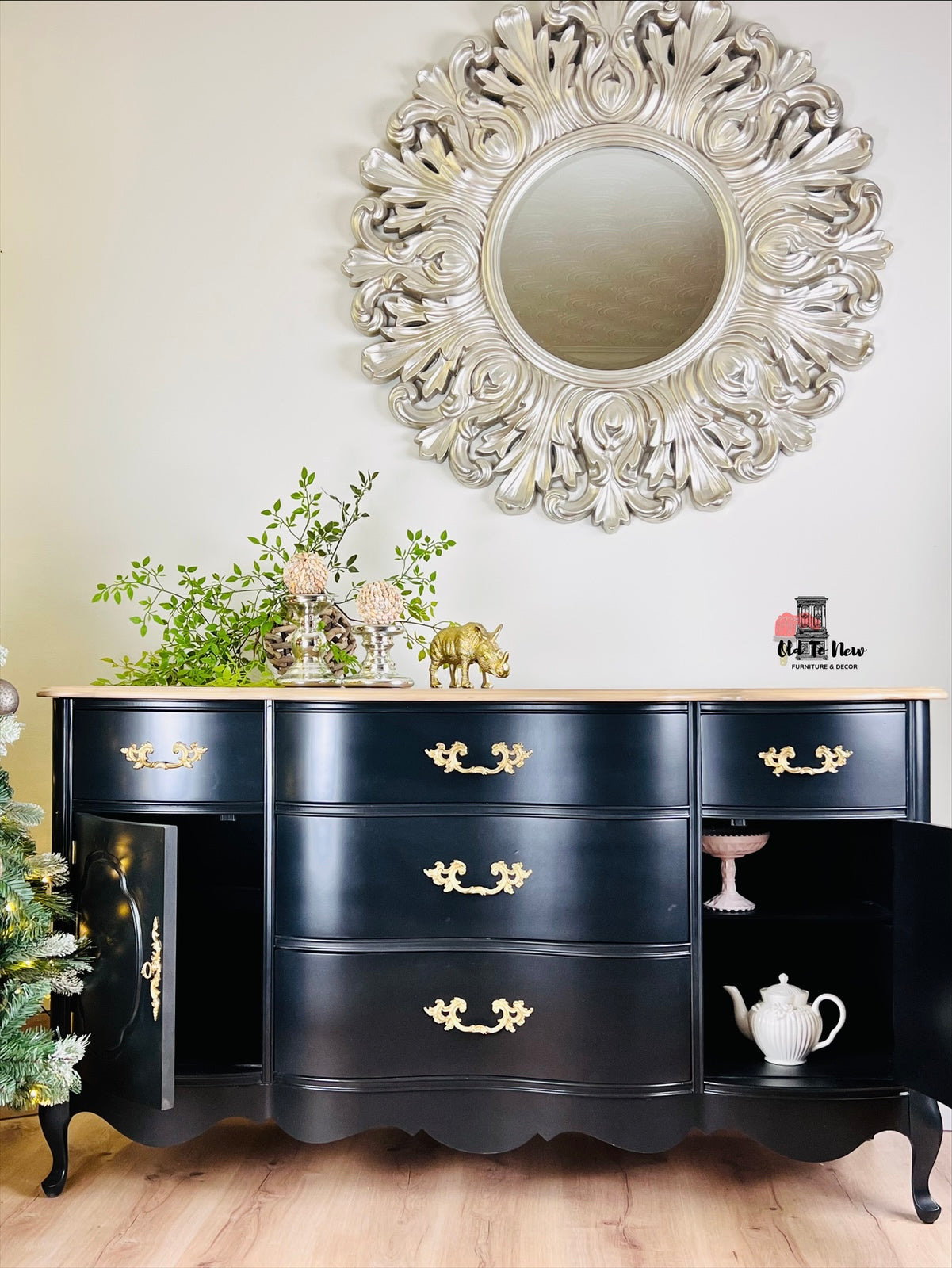 Black dresser with gold handles in a room with decorative mirror and plants.