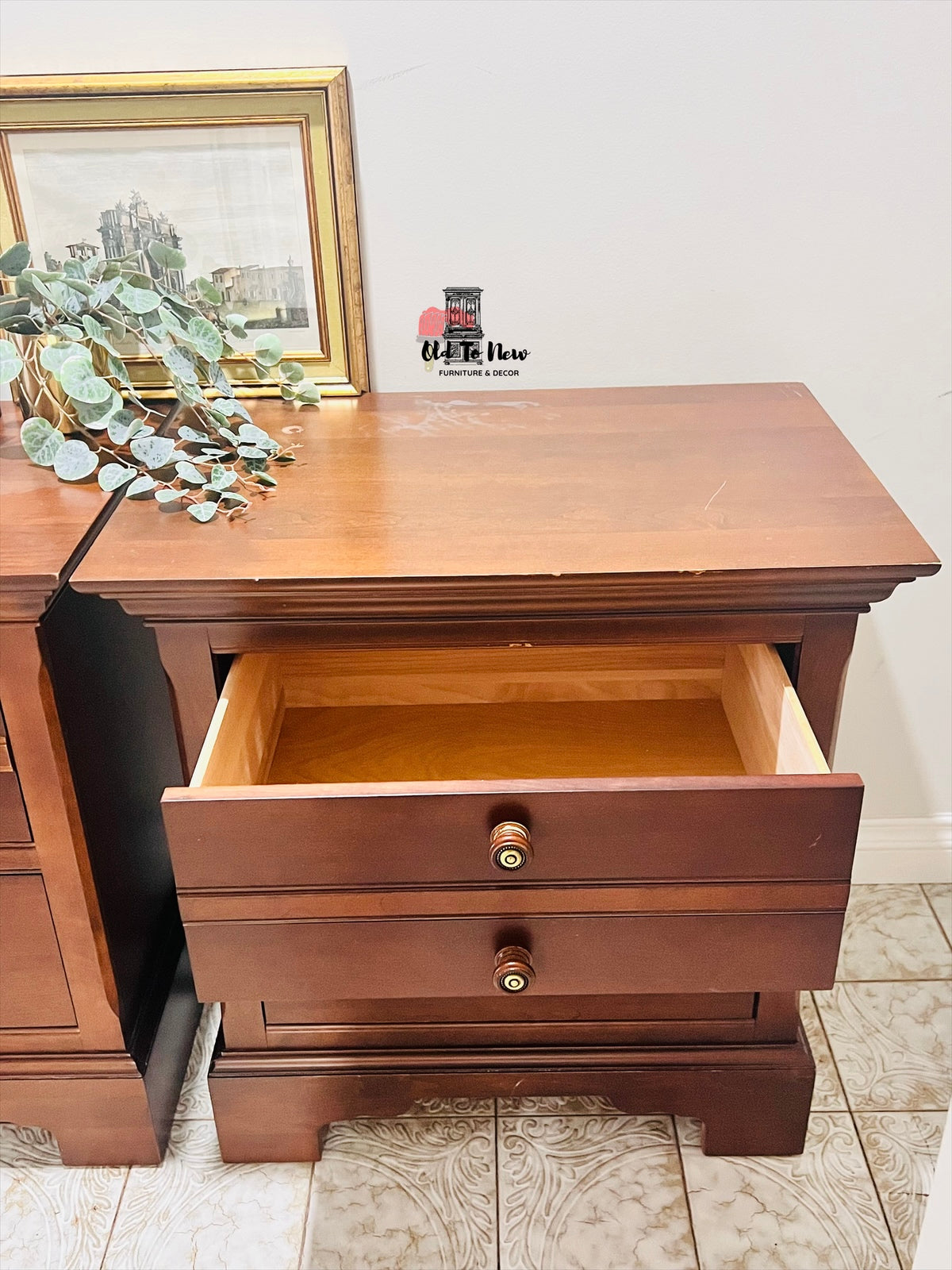 Wooden nightstand with an open drawer, framed picture, and plant in the background. Old to New Furniture & Decor, Canada