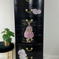 Black dresser with floral and decorative graphics on a white floor and light gray wall.