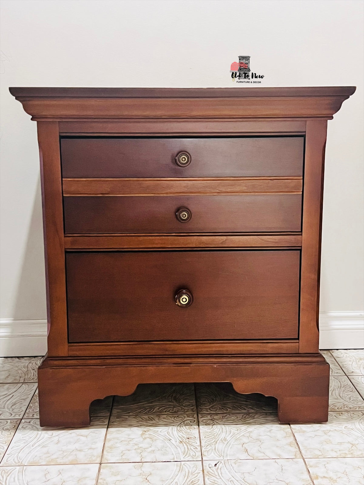 Wooden end table with three drawers on a tiled floor.