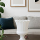 “Single white milk glass pedestal vase with a scalloped edge displayed on a dark wood coffee table in a minimalist modern living room with abstract wall art and neutral-toned sofa.”