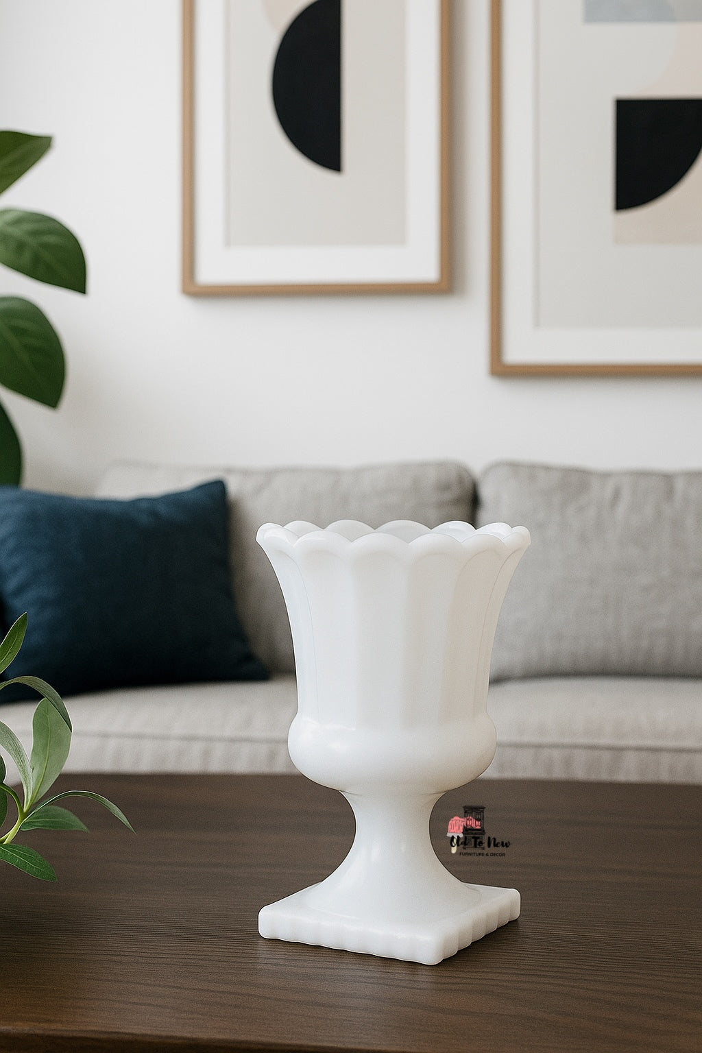“Single white milk glass pedestal vase with a scalloped edge displayed on a dark wood coffee table in a minimalist modern living room with abstract wall art and neutral-toned sofa.”