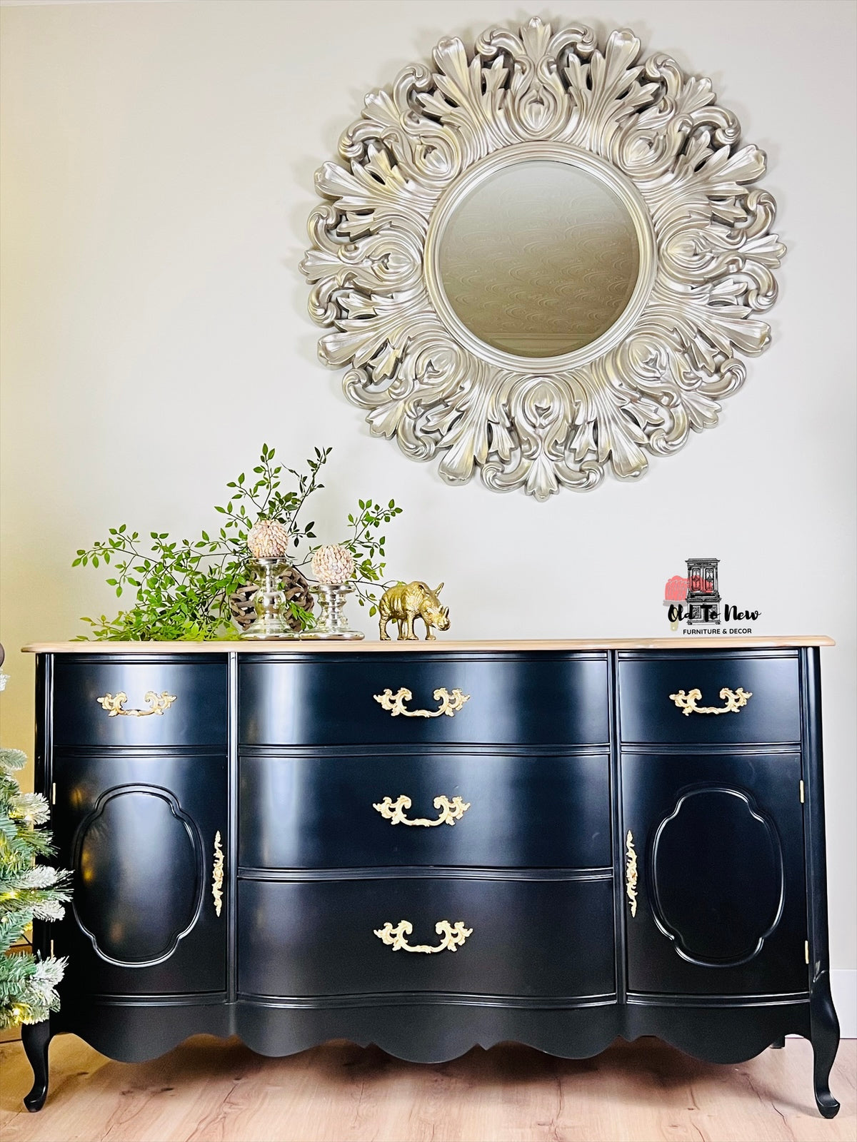 Black sideboard with gold handles against a white wall with a decorative mirror.